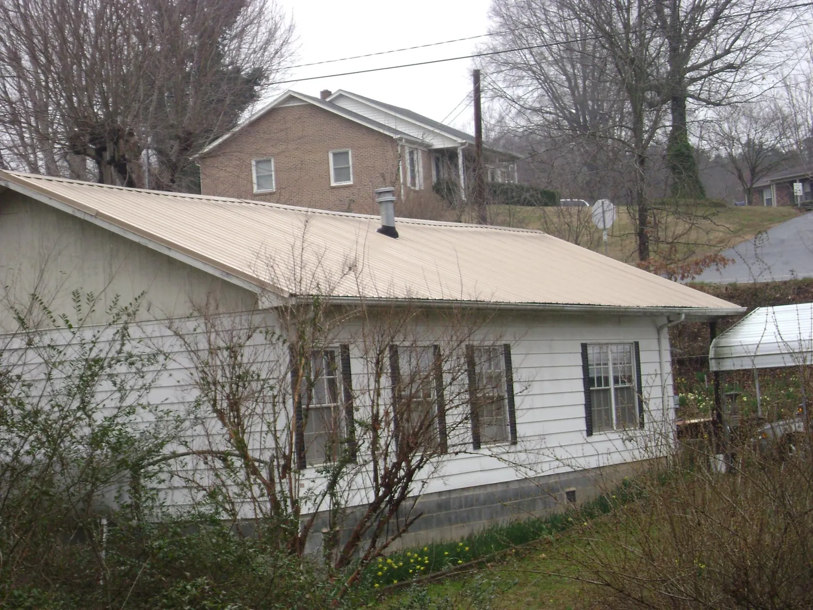 Tan metal roof on a white sided house set into a hillside — Commercial Roofing by Roofing Brothers in Taylor